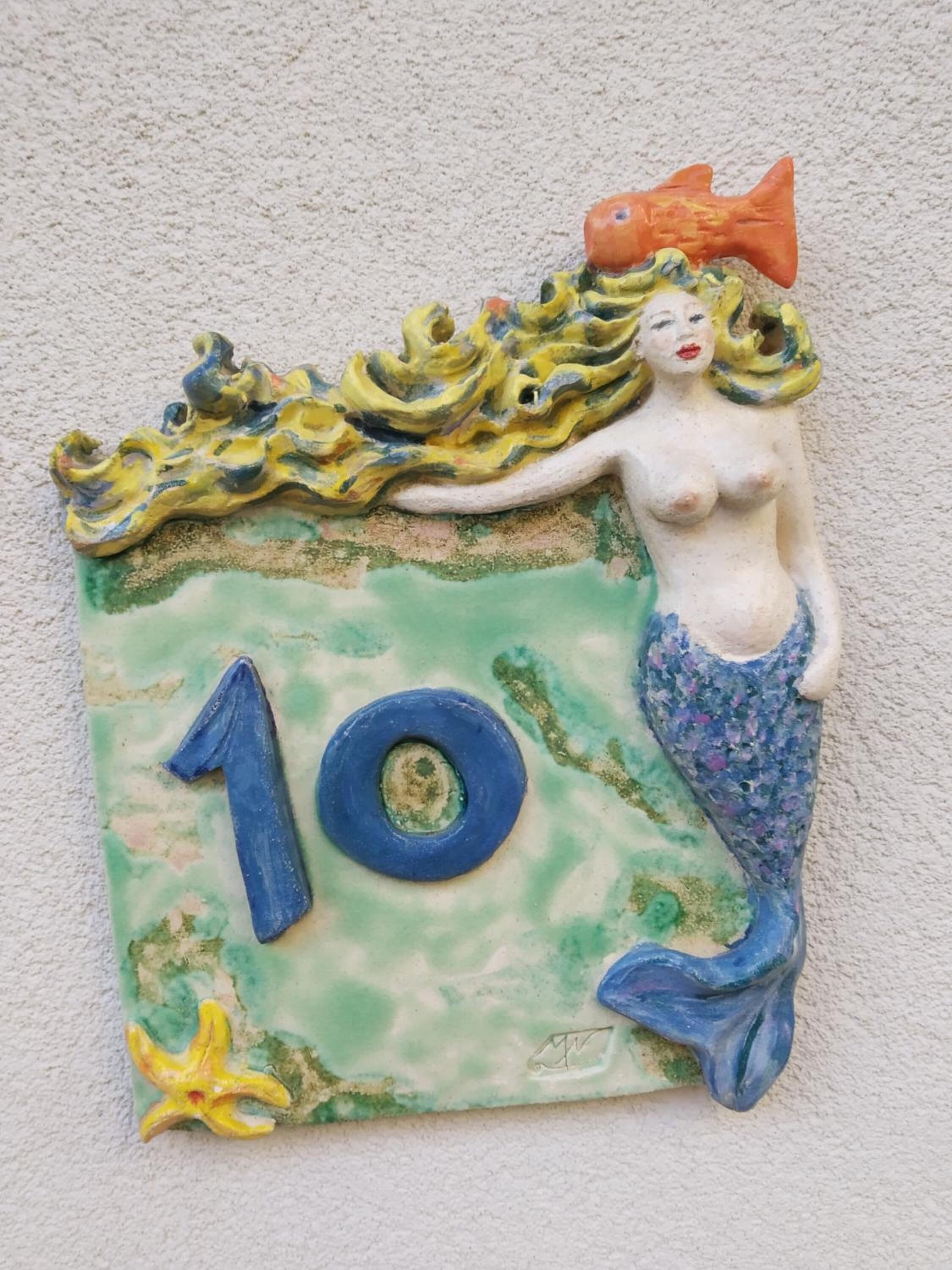 Un azulejo decorativo con una sirena, un pez y el número 10.