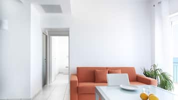 Un moderno salón con un sofá blanco, una mesa de centro de vidrio y una computadora portátil. Hay una planta en maceta y vistas al exterior.