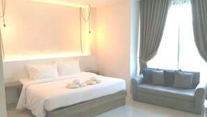 A modern hotel room with a large bed, a sofa, and a window with curtains.