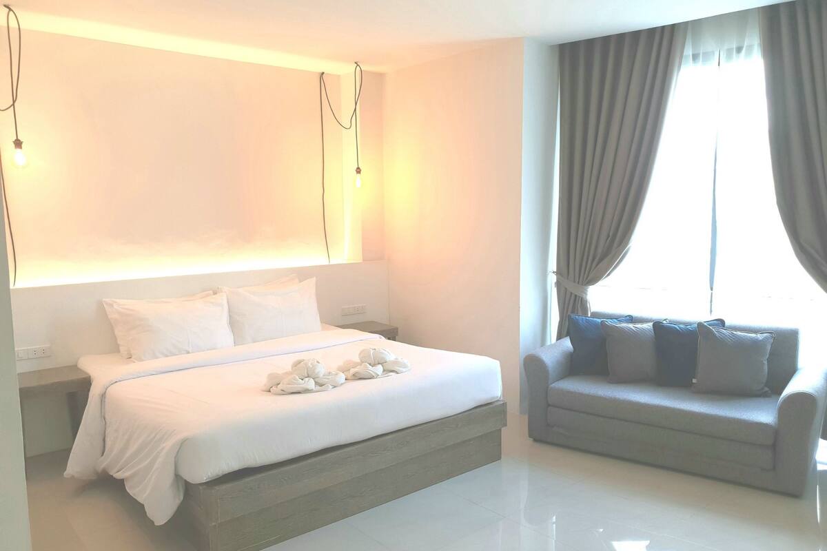 Una habitación de hotel moderna con una cama grande, un sofá y una ventana con cortinas.