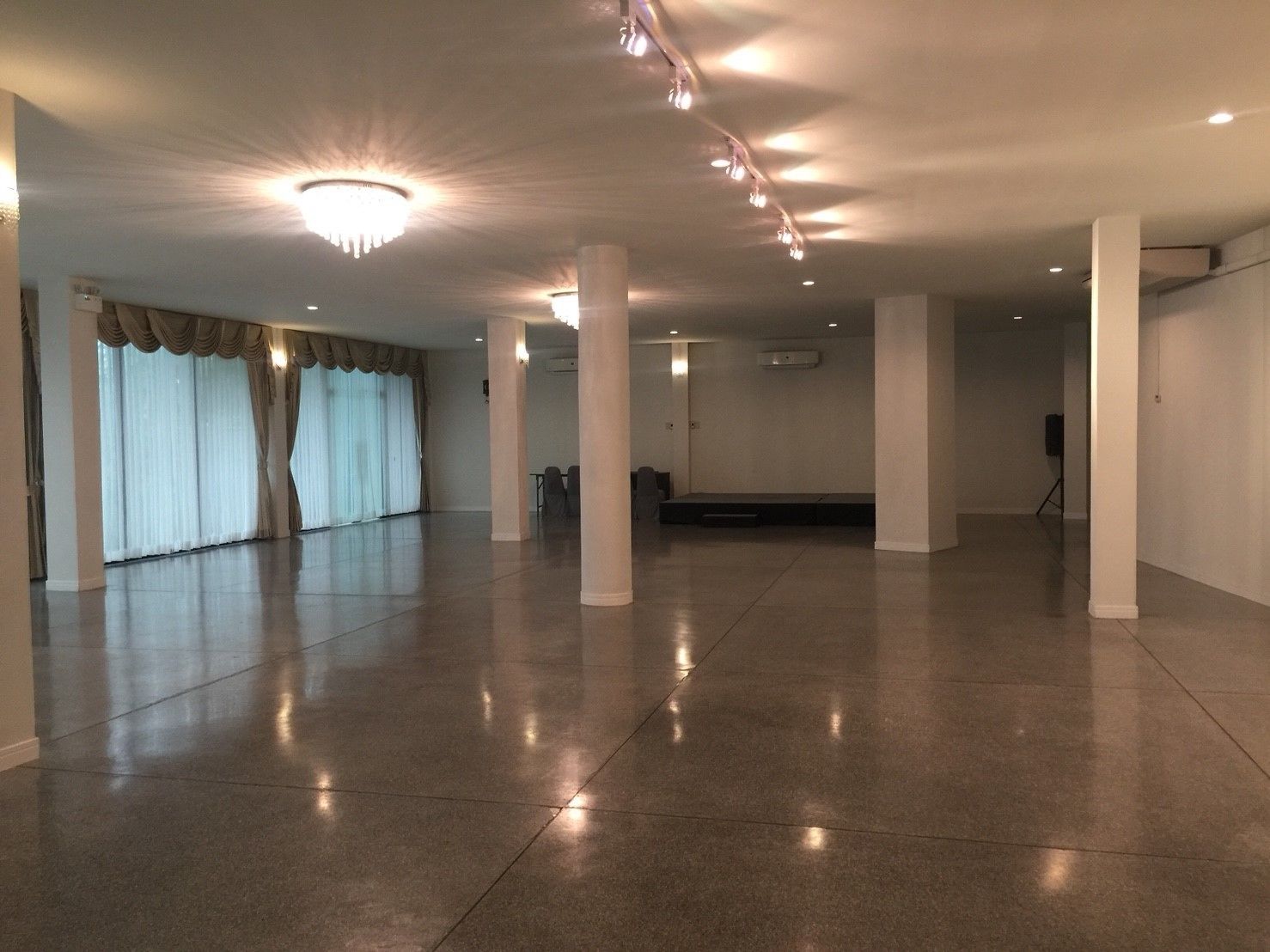 Un hallo amplio y luminoso con techo alto, ventanas grandes con cortinas y una zona de escenario.