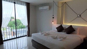 A hotel room with a large bed, a view of greenery outside, an air conditioning unit, and a modern light fixture.