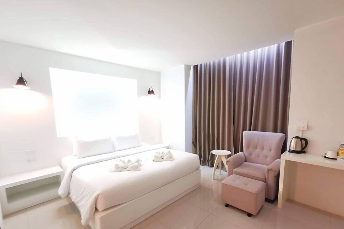 Una habitación de hotel moderna con una cama grande, un área de descanso con una silla y reposapiés, una mesita auxiliar y una ventana con cortinas.
