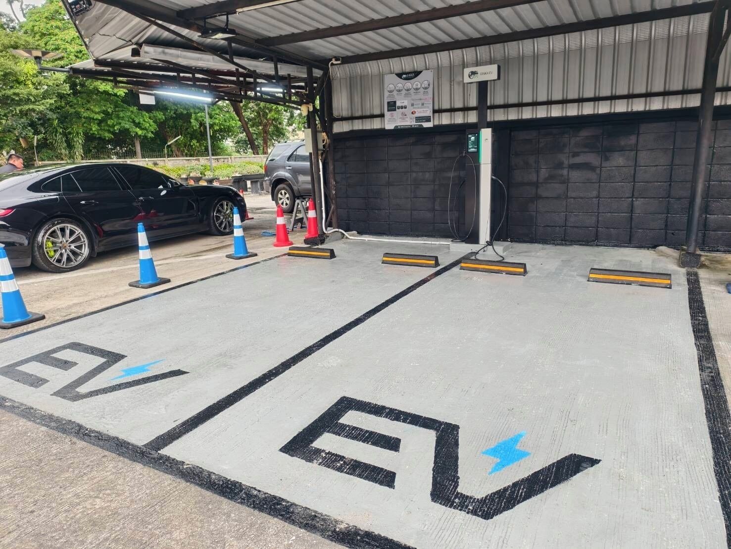 Une borne de recharge pour véhicules électriques, dotée d’un espace abrité, avec une voiture et des cônes de signalisation.