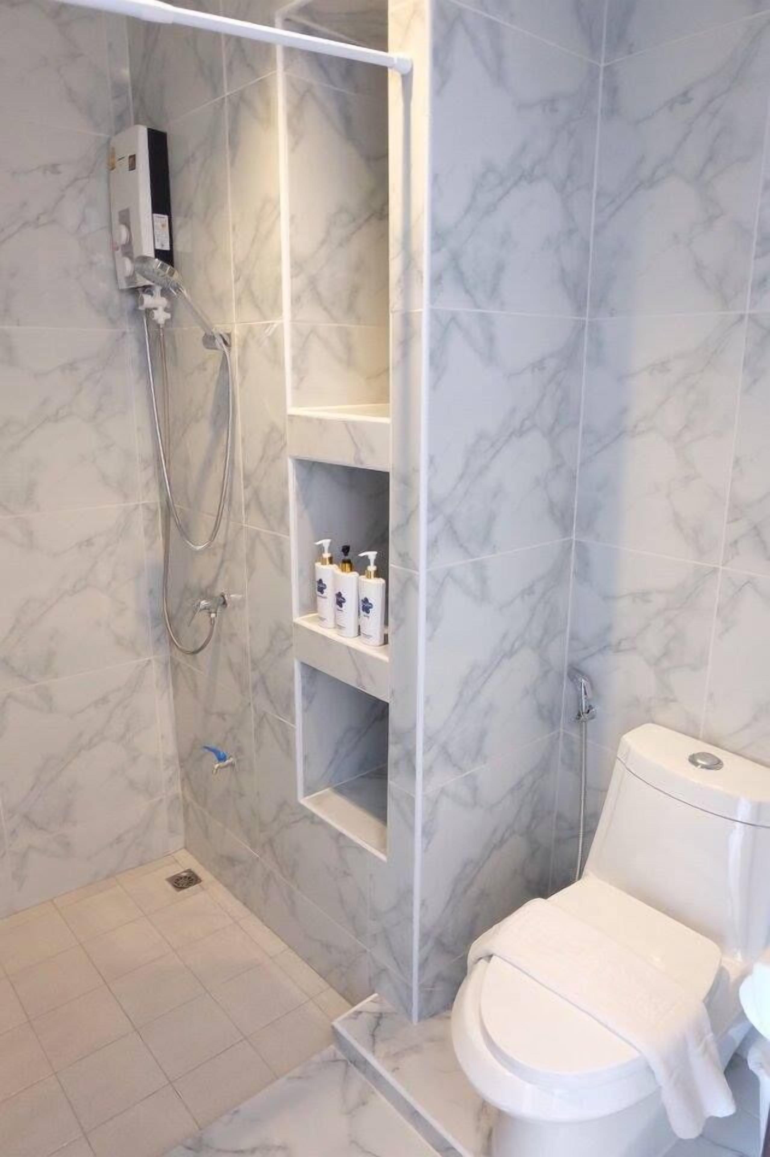 A bathroom with a shower, toilet, and marble tiles.