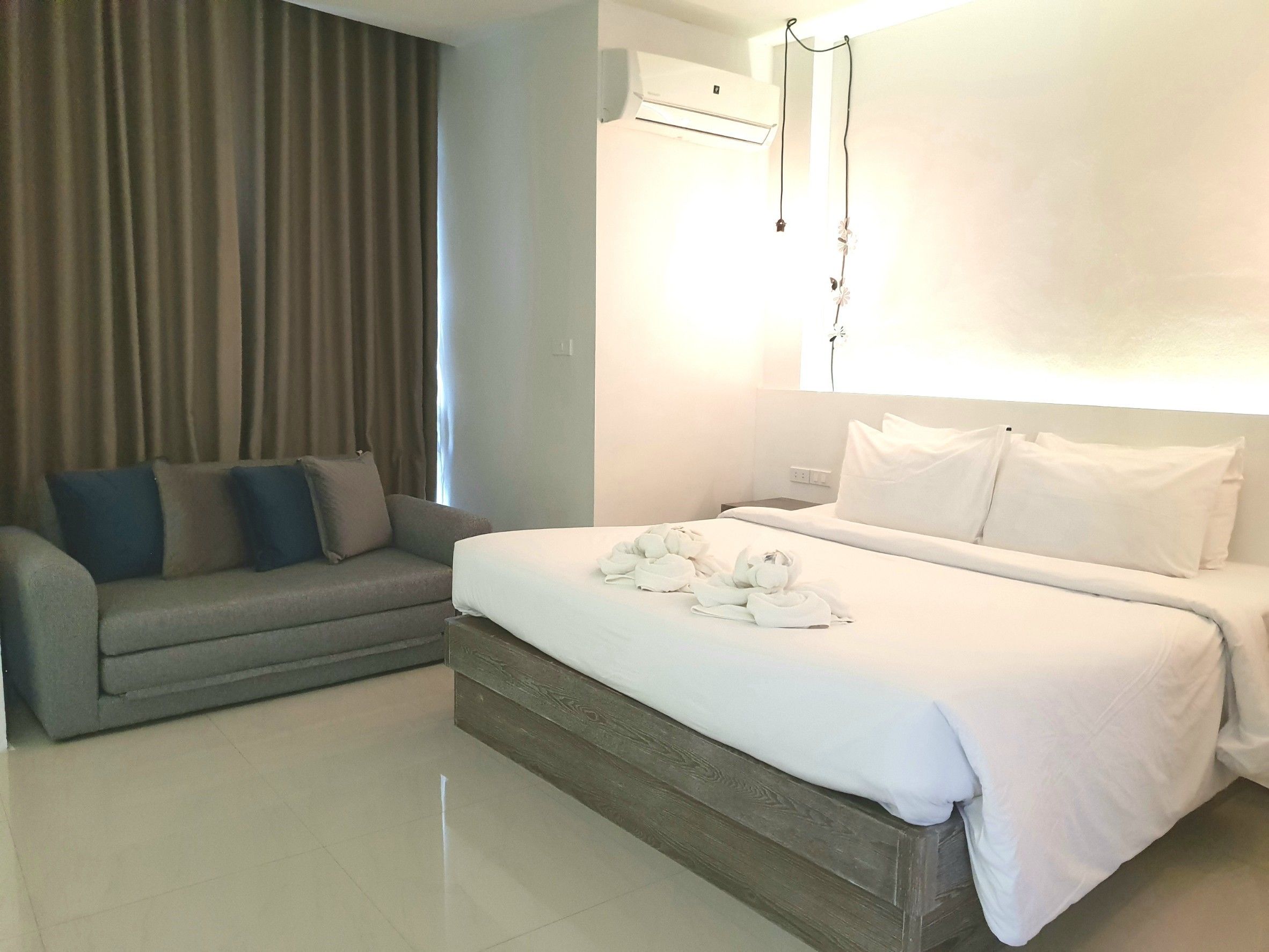 A hotel room with a bed, a sofa, and a wall-mounted air conditioner.