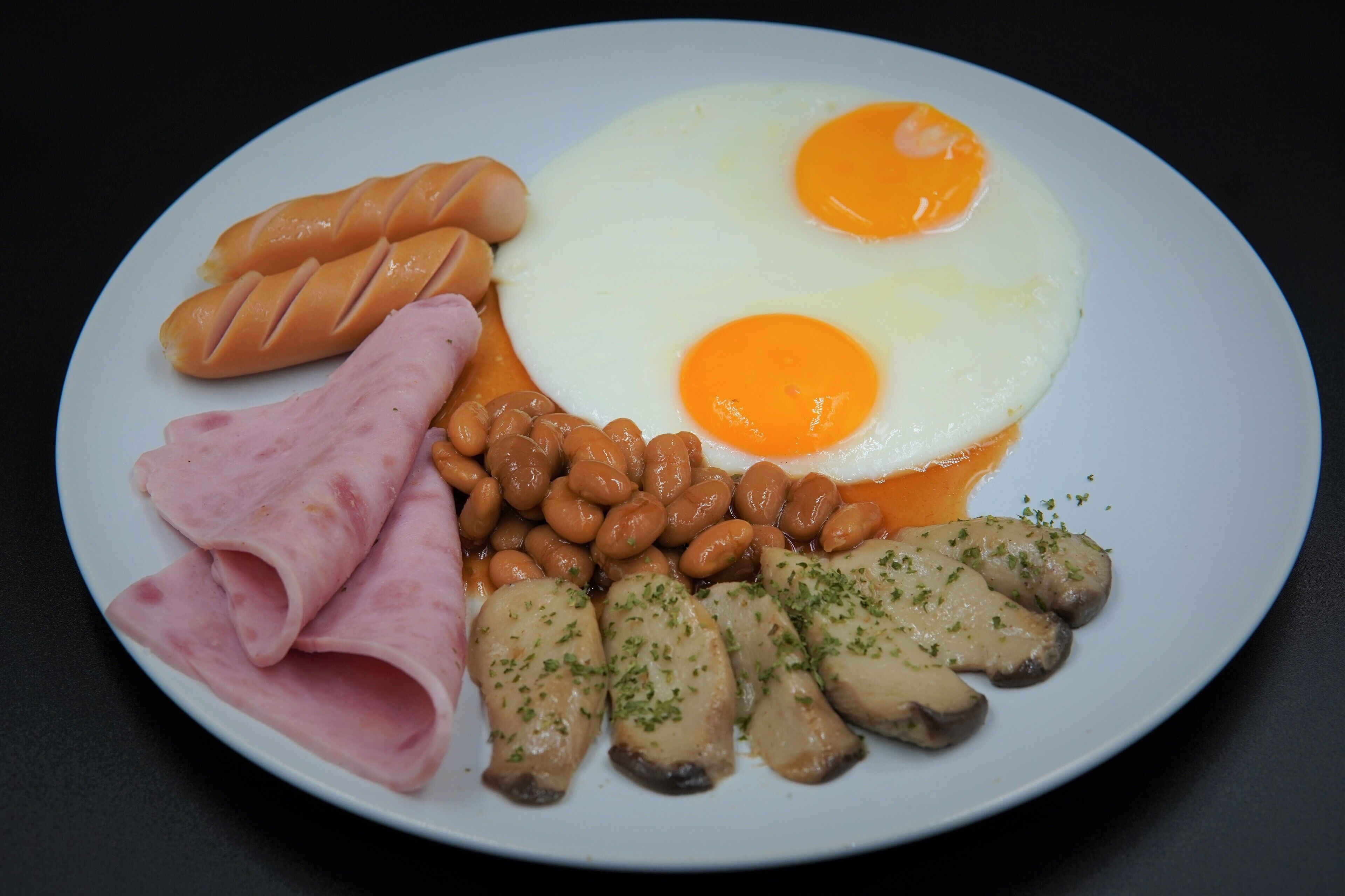 A plate with eggs, sausages, beans, ham, and mushrooms.