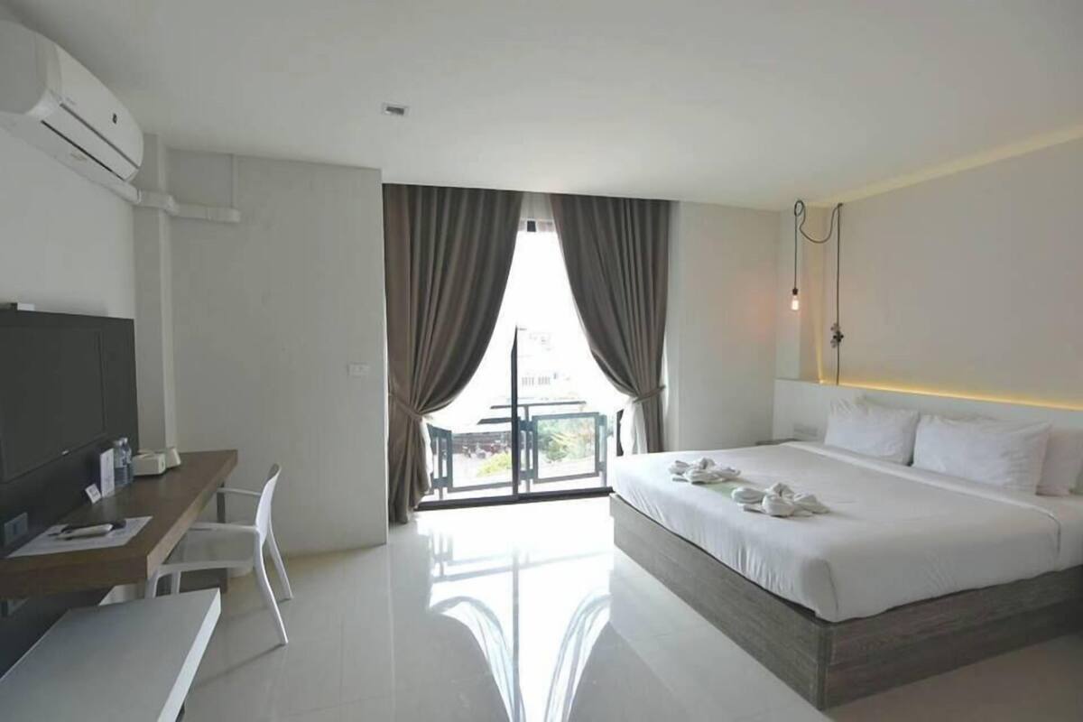 Una habitación de hotel moderna con una cama grande, un escritorio con silla y un balcón con cortinas.
