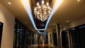 A modern hotel corridor with a central chandelier, glass doors, and a polished floor.
