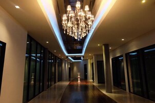Un pasillo moderno de hotel con una lámpara central de candelabro, puertas de vidrio y un suelo pulido.