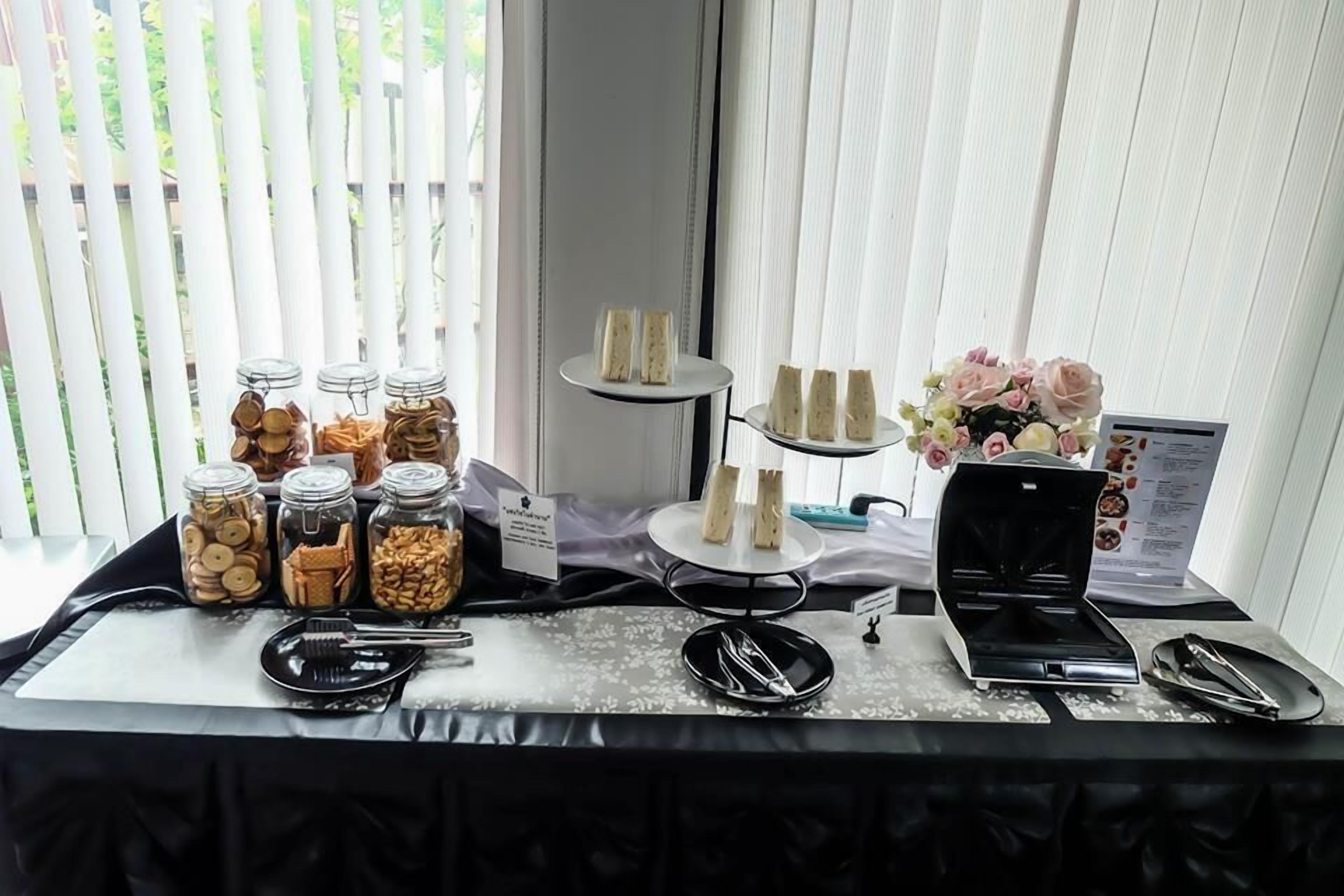 Een buffet met diverse etenswaren, waaronder potten met noten en koekjes, een taartplateau met cupcakes en een koffieapparaat.