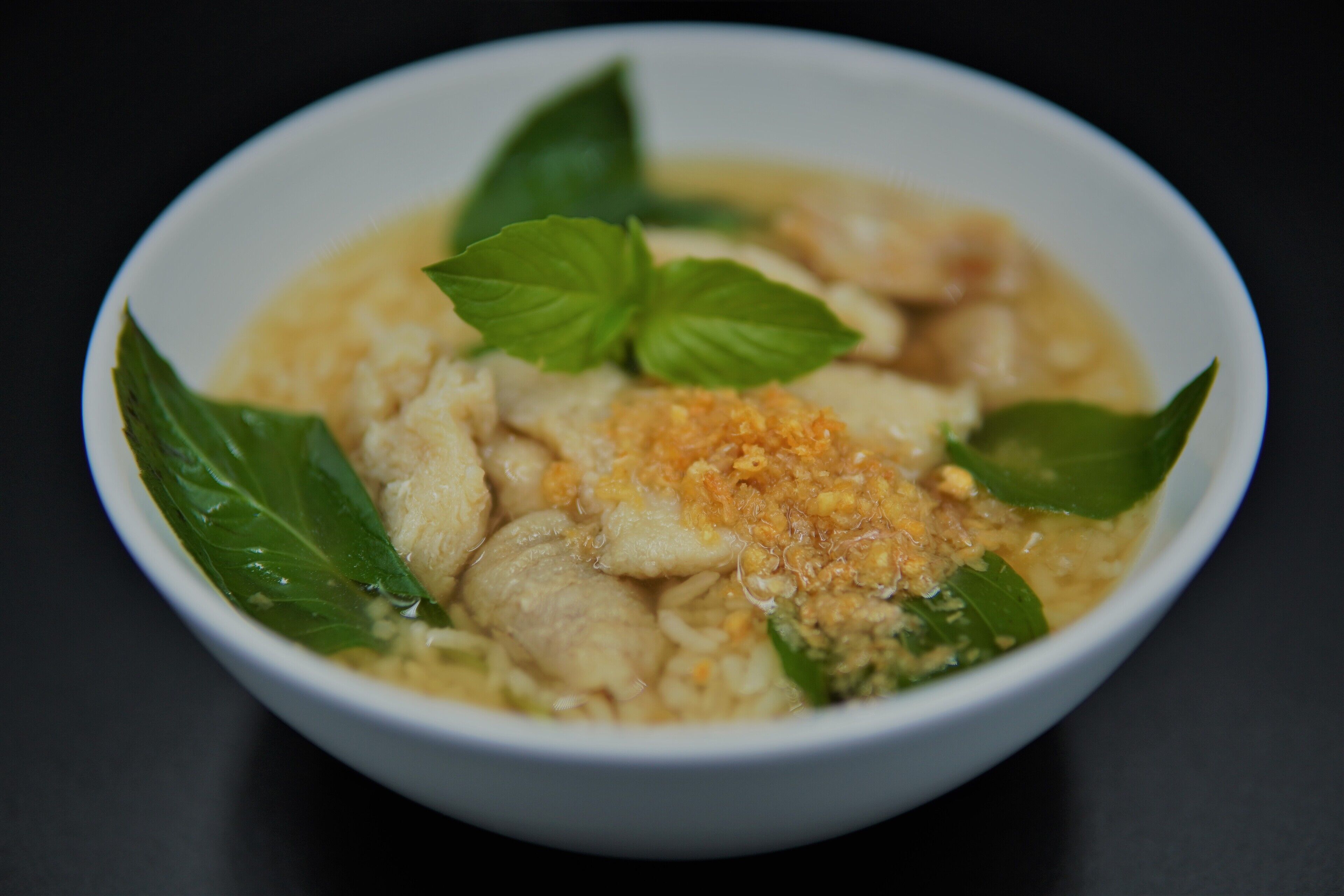A bowl of soup with noodles, chicken, and a garnish of green leaves and a crispy topping.