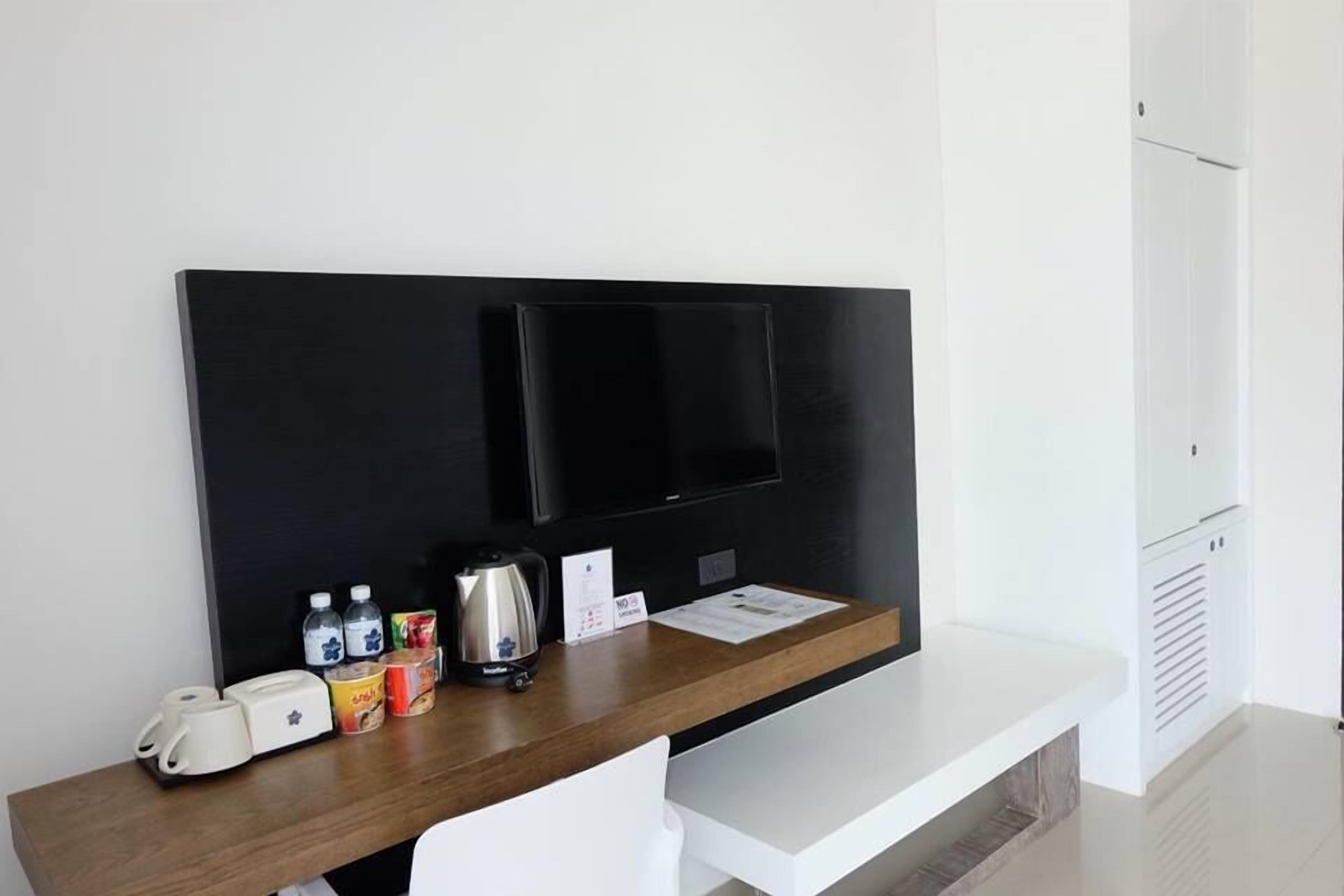 Una habitación de hotel moderna con un escritorio de madera, un televisor de pantalla plana, un hervidor de agua y una pequeña selección de alimentos para el desayuno.
