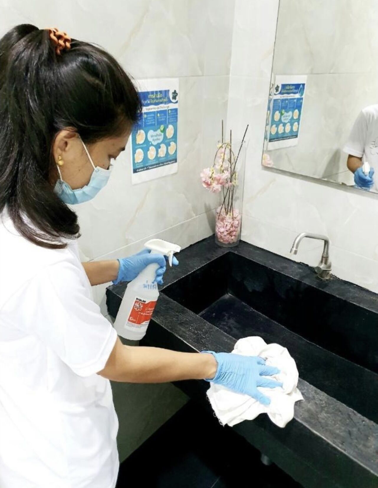 Una persona limpiando un lavabo negro con un pulverizador y un paño.