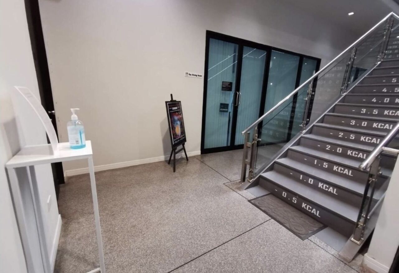 Un moderno vestíbulo de hotel con una escalera que indica las calorías quemadas, una pequeña mesa con una botella de agua y un expositor de carteles.