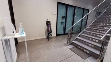 Un moderno vestíbulo de hotel con una escalera que indica las calorías quemadas, una pequeña mesa con una botella de agua y un expositor de carteles.