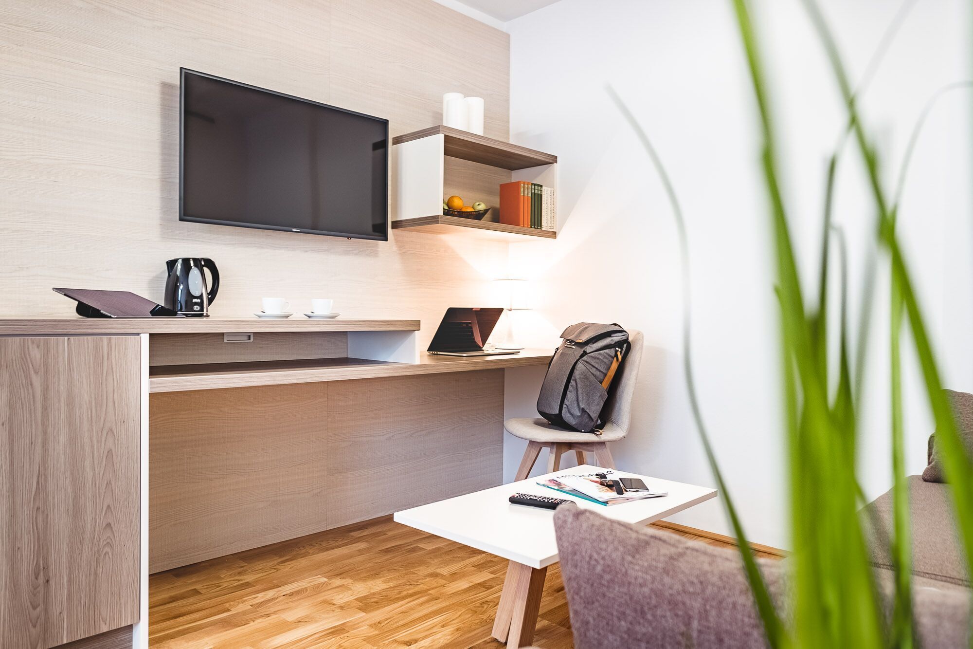 A modern hotel room with a flat-screen TV, a laptop, a coffee maker, and a small table with a remote control.