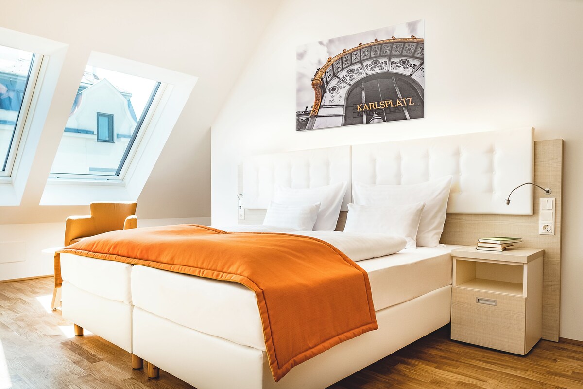 A modern bedroom with a white bed, orange throw, and a cityscape poster on the wall.