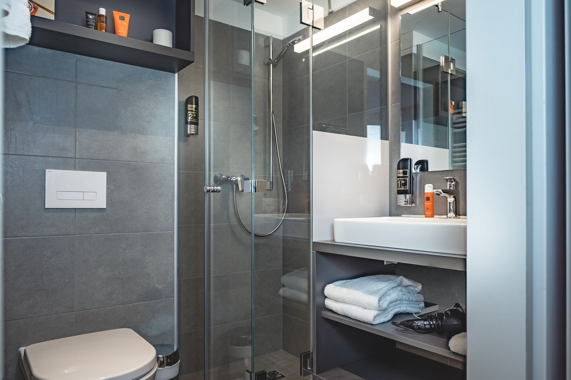 A modern bathroom with a glass-enclosed shower, a white toilet, and a vanity with a mirror.