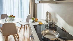 A modern kitchen with a stove, a dining table with chairs, and a fruit bowl. -  OLIVER urban I Self check-in Apartments (Vienna)