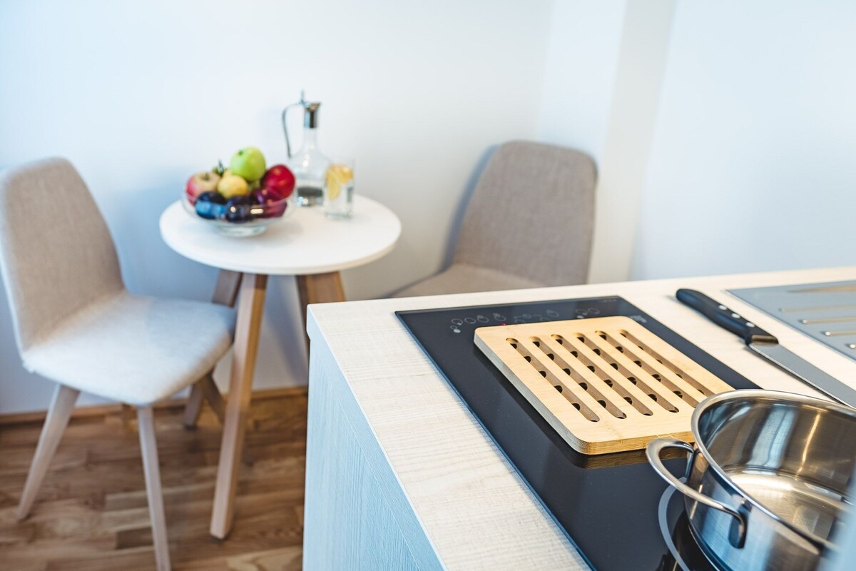 A modern kitchen with a built-in stove, a cutting board, and a stainless steel pot.