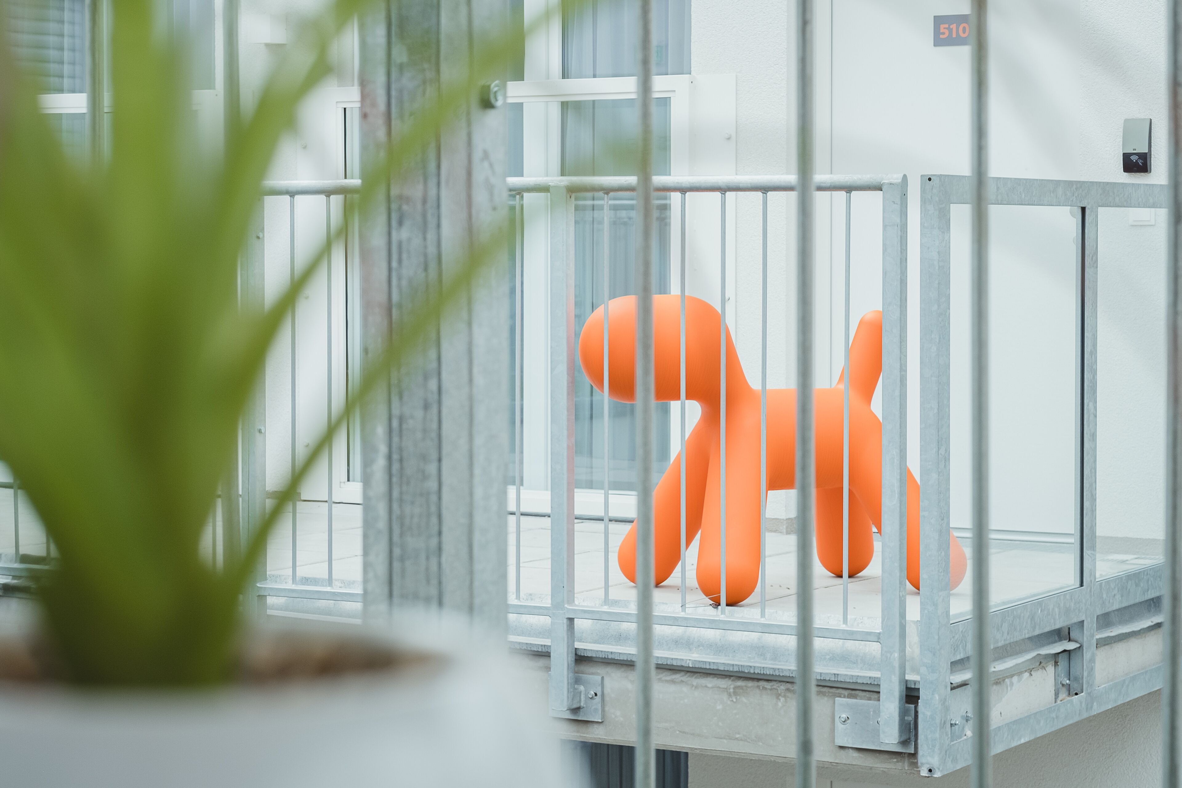 A room with a metal railing, a potted plant, and a bright orange chair.