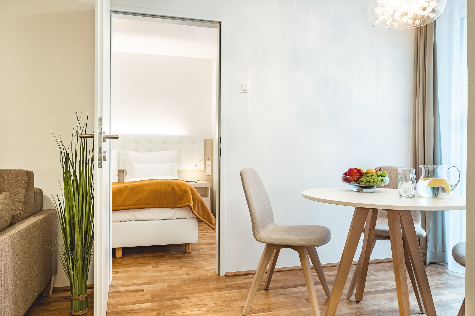 Une chambre d’hôtel moderne, équipée d’un lit, d’une table à manger avec des chaises, d’un vase de fleurs et offrant une vue sur la ville.