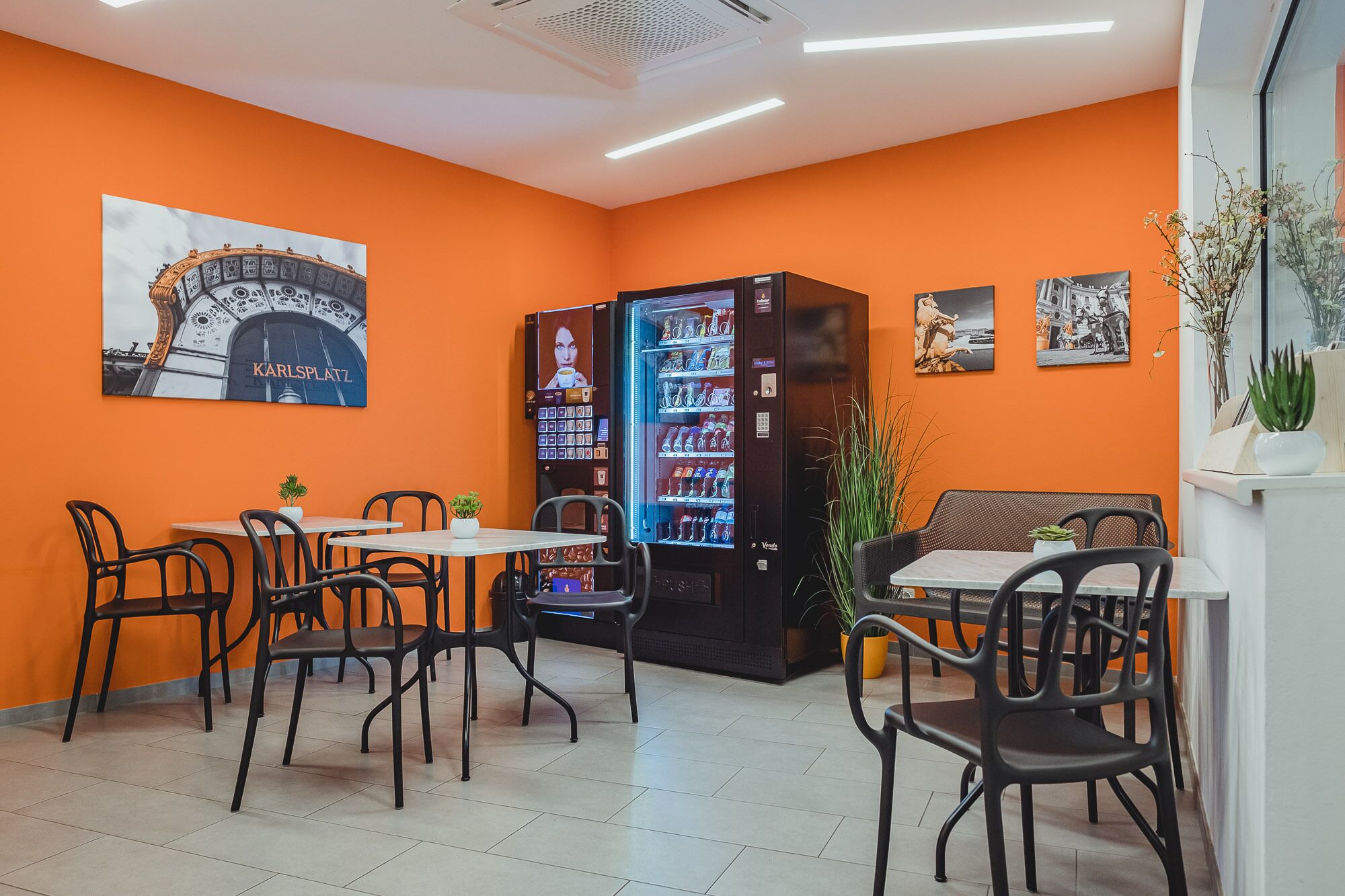 A cafe with orange walls, black chairs, and a vending machine.