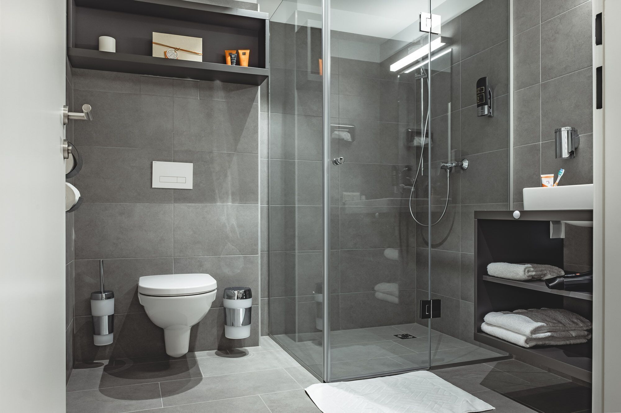 Un baño moderno con ducha de vidrio, inodoro y zona de lavamanos con toallas.