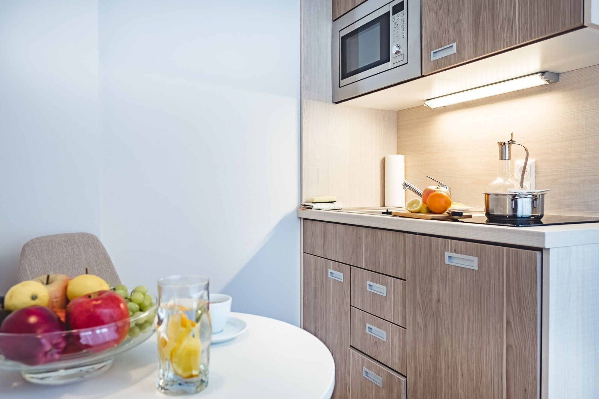 A modern kitchen with wooden cabinets, a microwave, a kettle, and a fruit bowl on the counter.