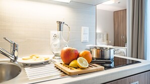 A modern kitchen with a stainless steel sink, a glass water dispenser, a cutting board with fruits, and a stove. -  OLIVER urban I Self check-in Apartments (Vienna)