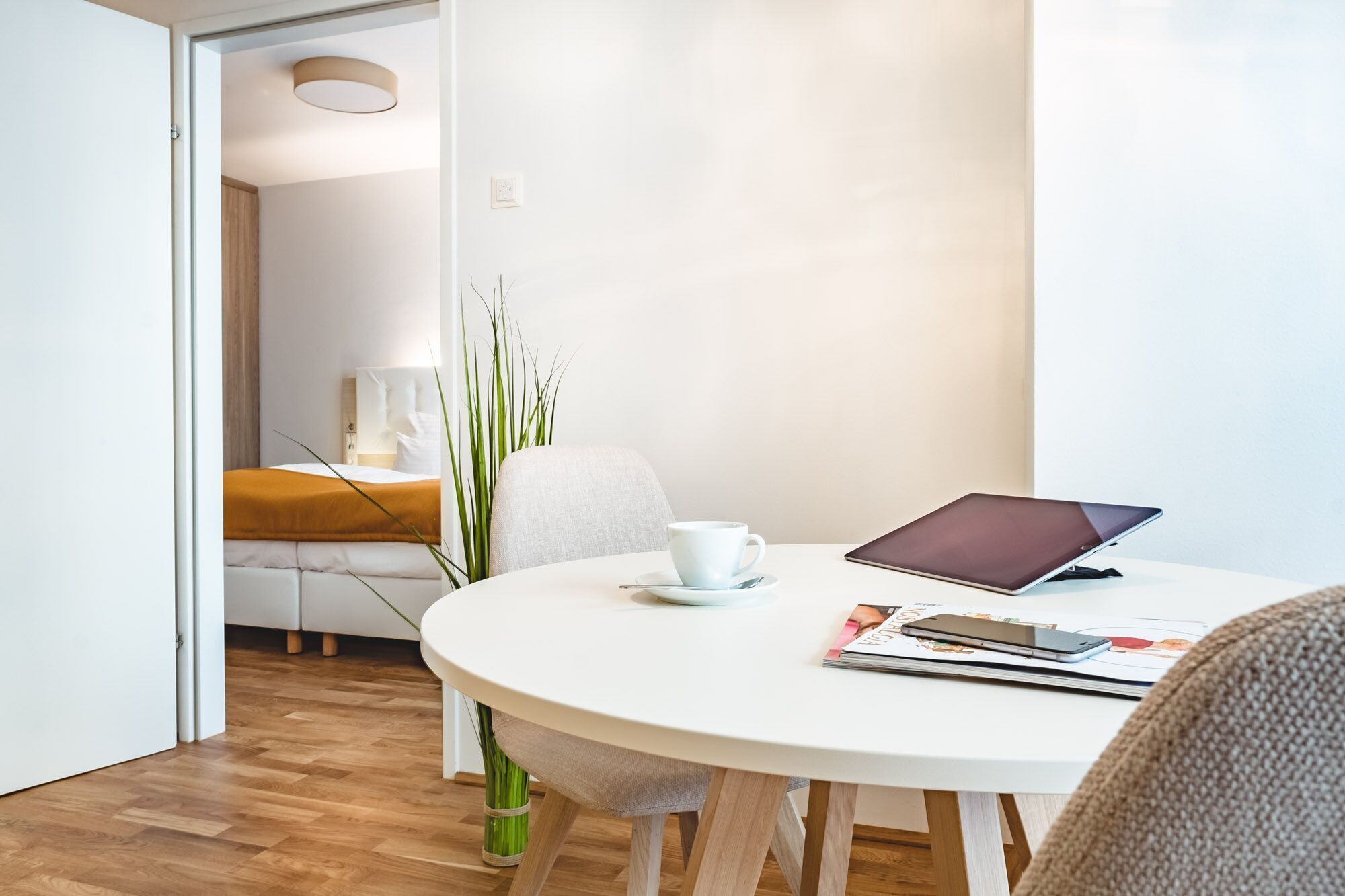 Una habitación moderna y minimalista con una mesa redonda blanca, una computadora portátil, una taza y una revista.