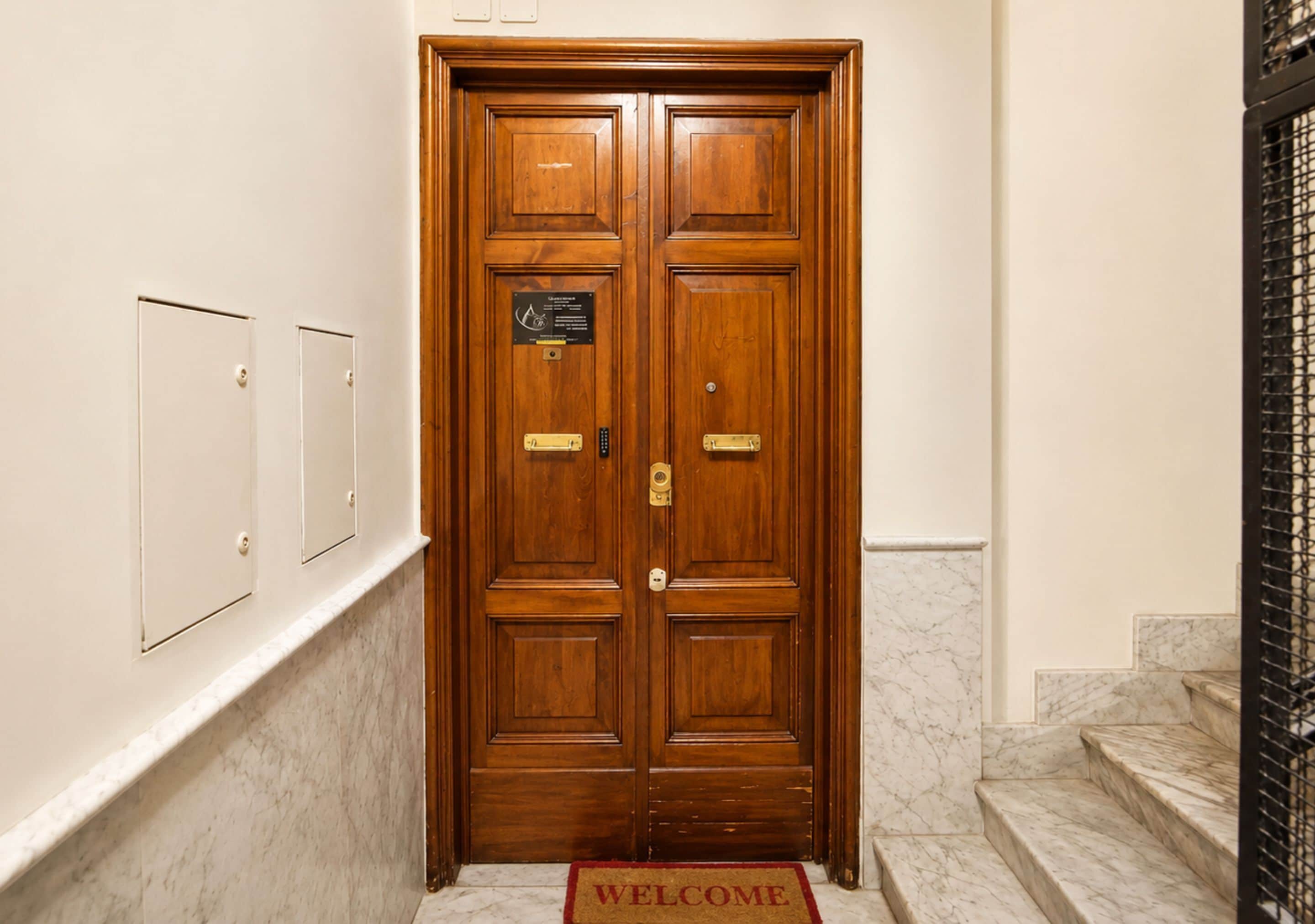 Una porta in legno a due battenti con una targa, un tappeto d'ingresso e una scala in marmo.