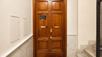 Una porta in legno a due battenti con una targa, un tappeto d'ingresso e una scala in marmo.