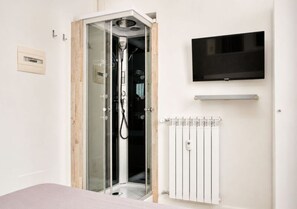 A bathroom with a glass-enclosed shower, a mounted television, and a white radiator. - Inside Roma Rooms by DOT Suites (Rome)