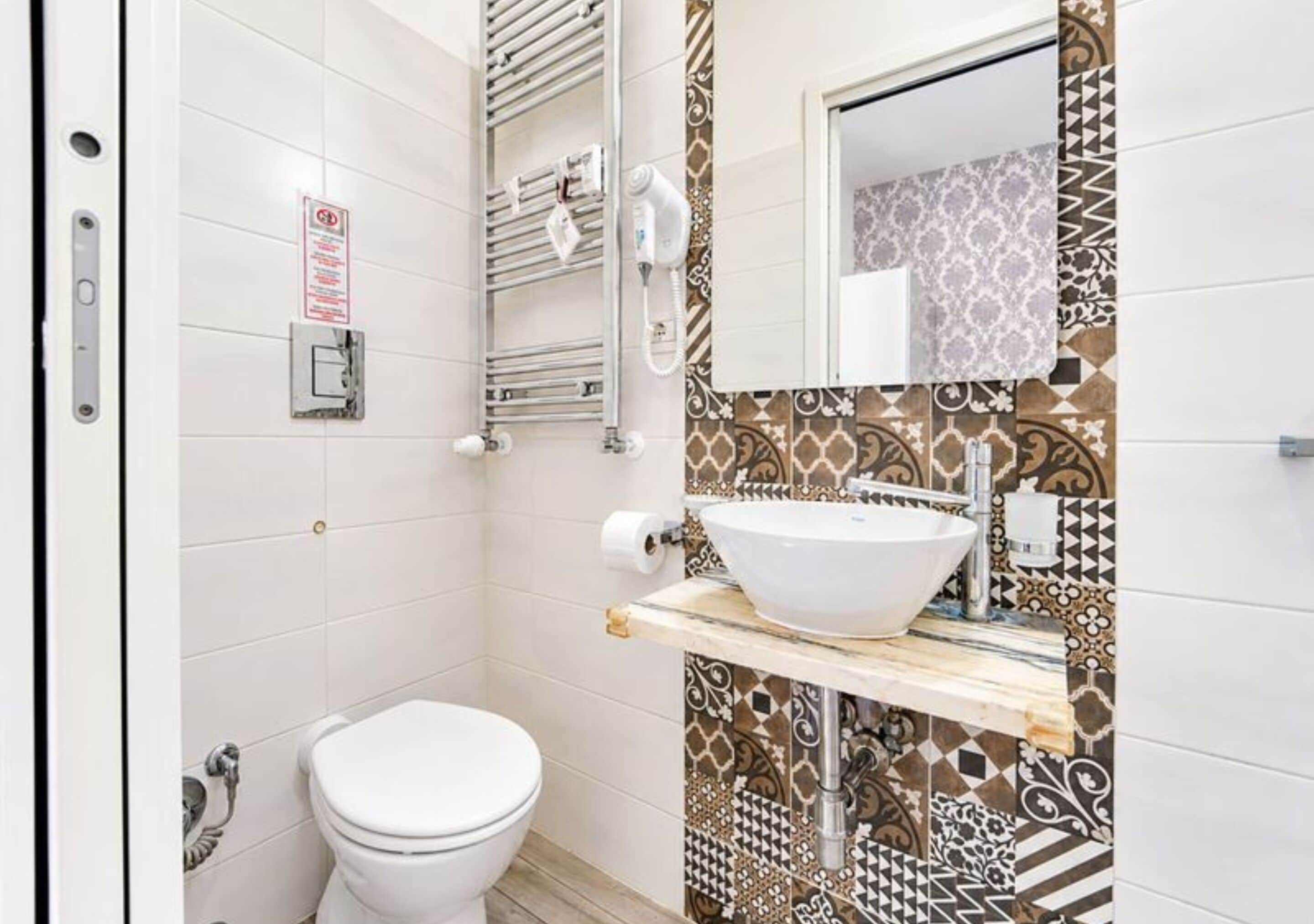 Een badkamer met een wit toilet, een wastafel met een marmeren aanrechtblad en behangtegels op de muren.