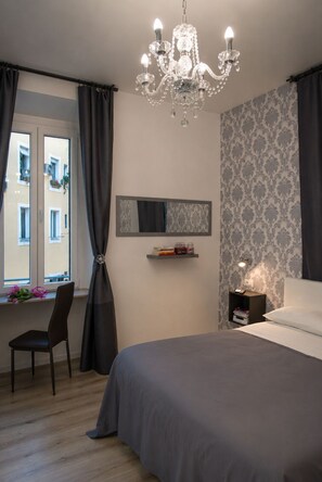 A bedroom with a bed, a chair, a desk, a chandelier, a mirror, and a window with curtains. - Inside Roma Rooms by DOT Suites (Rome)