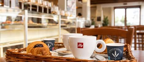 A breakfast setting with croissants, coffee cups, and a wicker tray on a table.