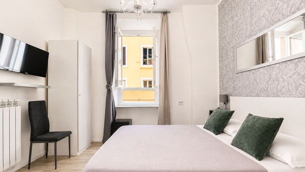 A modern bedroom with a bed, a chair, a television, and a window. - Inside Roma Rooms by DOT Suites (Rome)