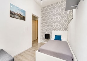 Une chambre à coucher comprenant un lit, une table de chevet, un téléviseur fixé au mur et une porte donnant sur une autre pièce.