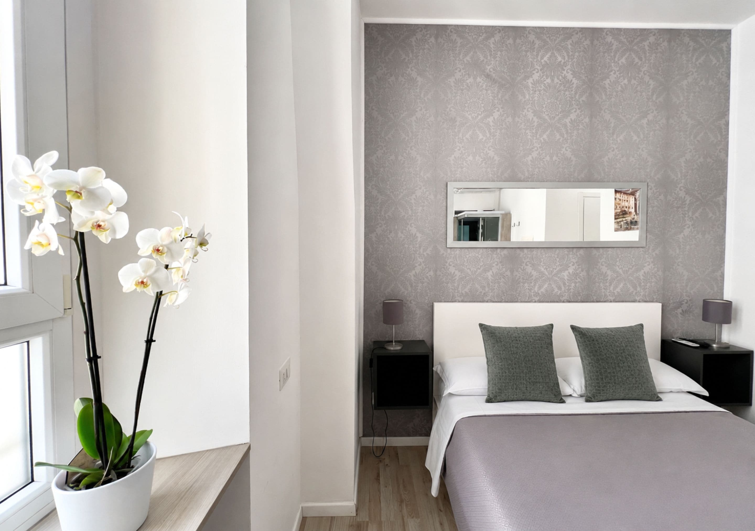 Una camera da letto moderna con un letto grande, due comodini, una lampada da comodino, uno specchio e un'orchidea in vaso.