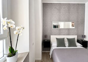 A modern bedroom with a large bed, two nightstands, a bedside lamp, a mirror, and a potted orchid. - Inside Roma Rooms by DOT Suites (Rome)