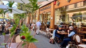 An outdoor café with tables and chairs, a building with a sign, and people dining. - Inside Roma Rooms by DOT Suites (Rome)