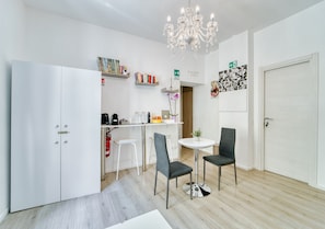 A modern kitchen with white cabinets, a dining area with two chairs, a chandelier, and a small table. - Inside Roma Rooms by DOT Suites (Rome)