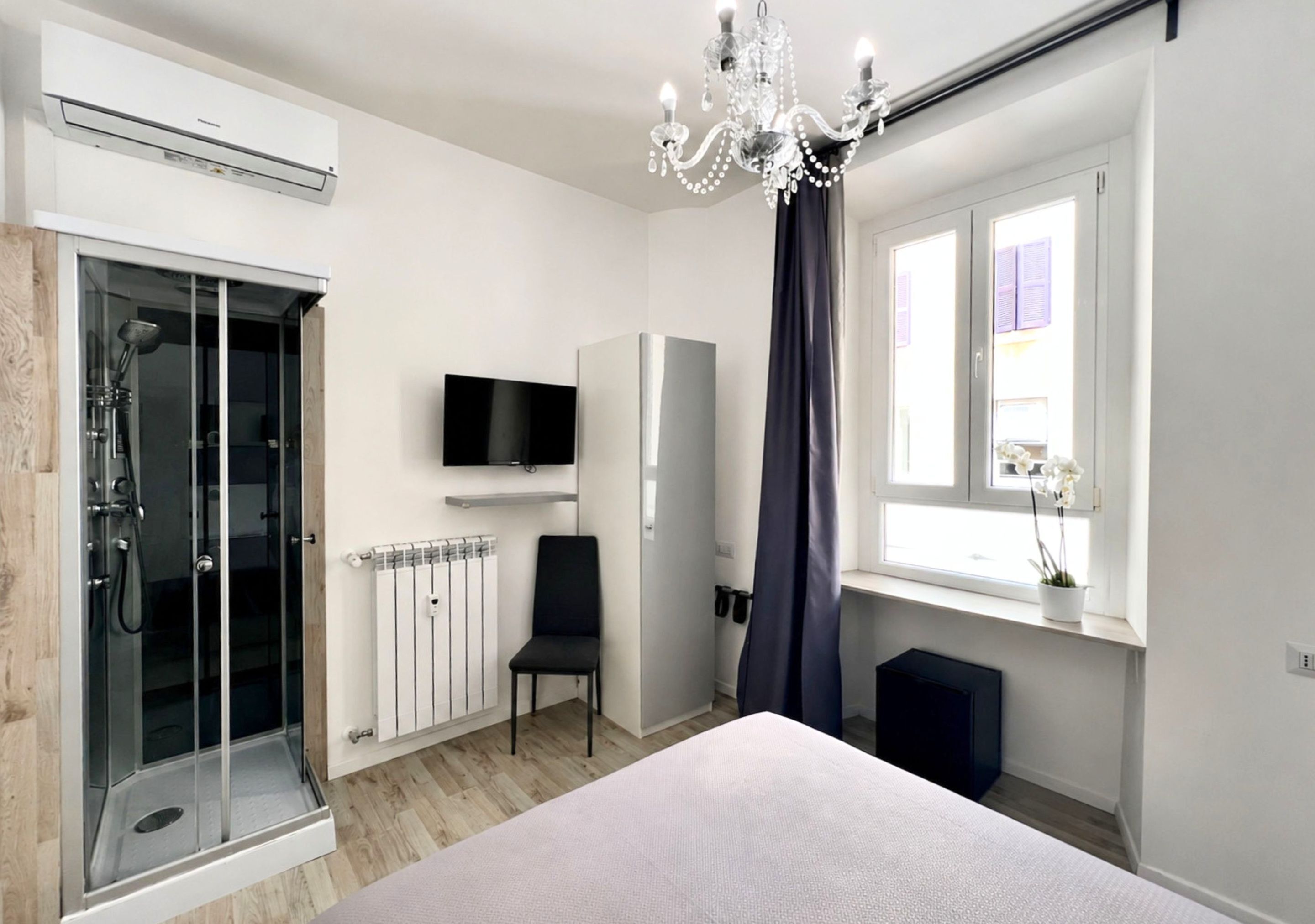 Une chambre moderne dotée d’une douche à parois de verre, d’un téléviseur à écran plat, d’un radiateur, d’une chaise et d’une fenêtre avec des rideaux.