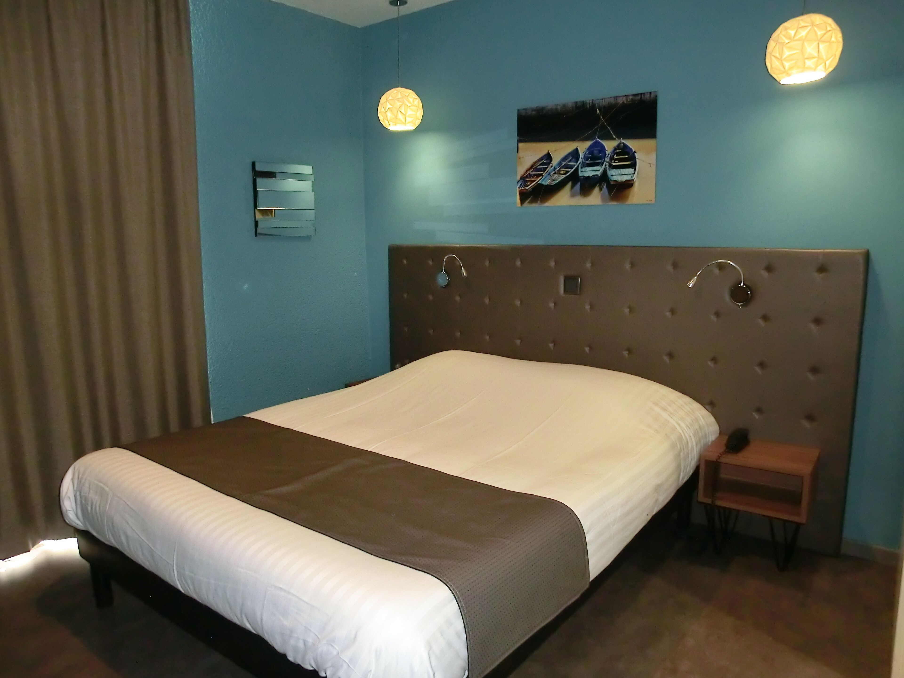 Ein modernes Hotelzimmer mit einem großen Bett, einer gepolsterten Kopfteil, einem kleinen Nachttisch und einer Wandleuchte.