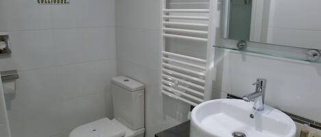 A modern bathroom with a toilet, bidet, and a sink with a glass shelf.