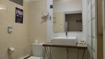A bathroom with a toilet, sink, and mirror. There is a poster on the wall and a hand dryer.