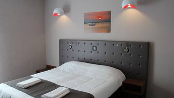 Una cama bien hecha con un cabecero gris, dos mesitas de noche y un cuadro colgado en la pared que muestra un atardecer sobre el agua.