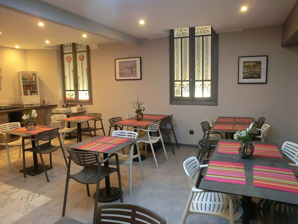 A dining area with tables and chairs, a kitchen area with cabinets, and a window with decorative glass. - Hôtel sur le Quai (Port-Vendres)